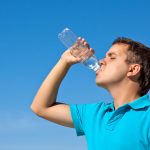 young male drinking water against blue sky